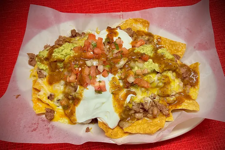 Our Super Nachos on a paper-lined plate with guacamole, sour cream, beans and salsa
